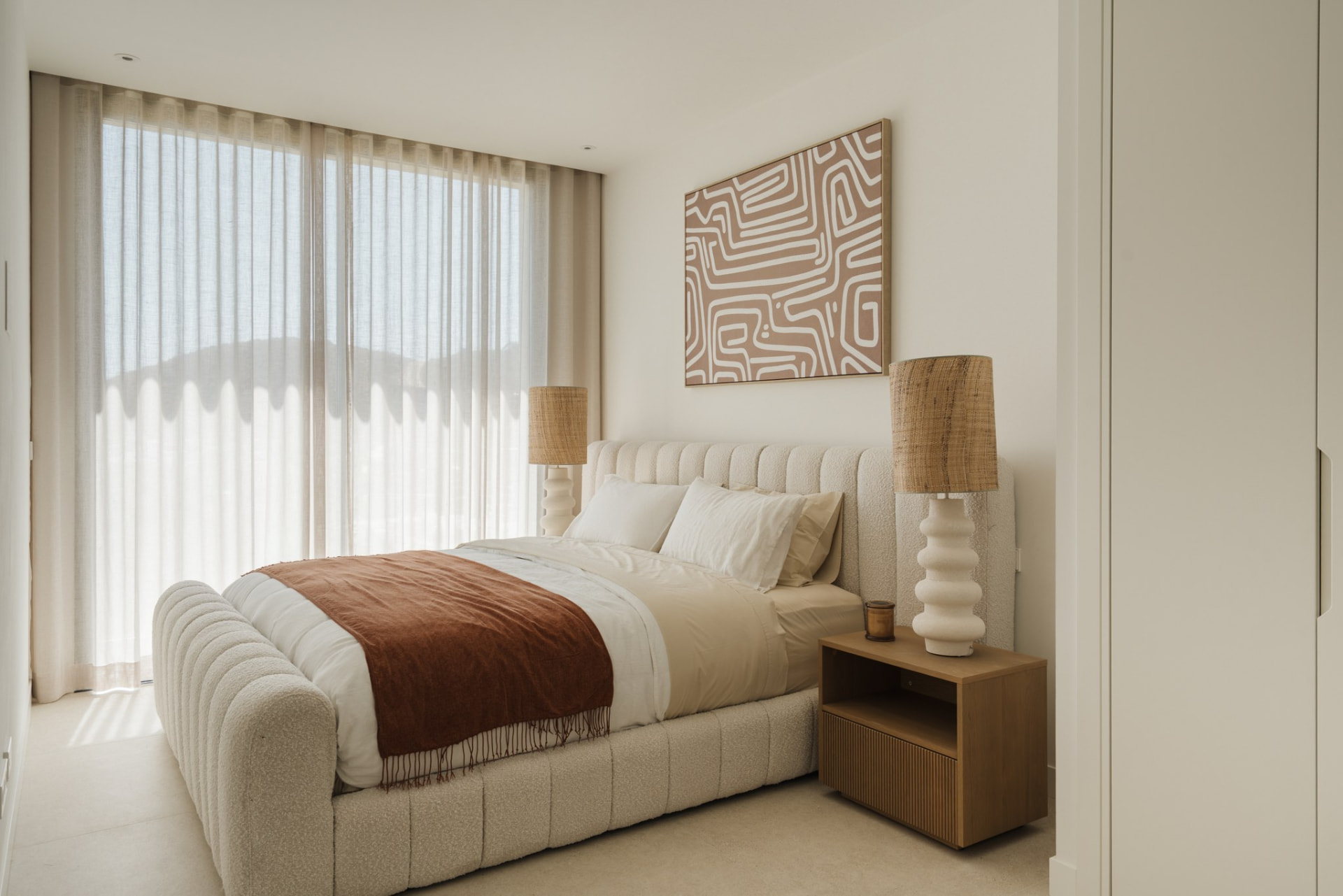 Guest bedroom with boucle bed, rattan lamps and sheer linen curtains